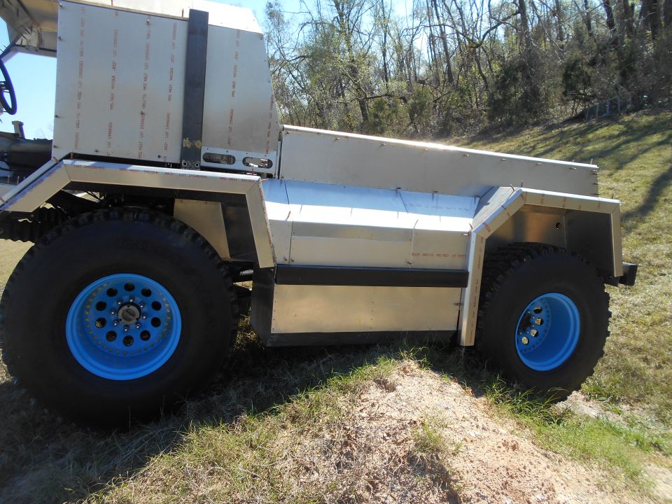 Custom silver vehicle with blue rims and large tires on a grassy hill.