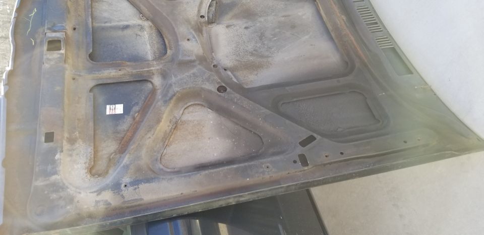 Underside of a car hood with rust and dirt.