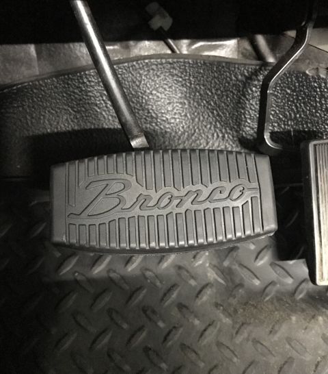 1995 Ford Bronco - A close-up view of a black rubber pedal cover with the word "Bronco" embossed in the center, installed on the floor of a vehicle.