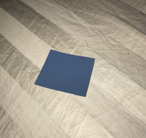 1995 Ford Bronco - A small, dark blue square swatch is placed on a striped fabric surface. The fabric has diagonal stripes of varying shades of gray and beige.