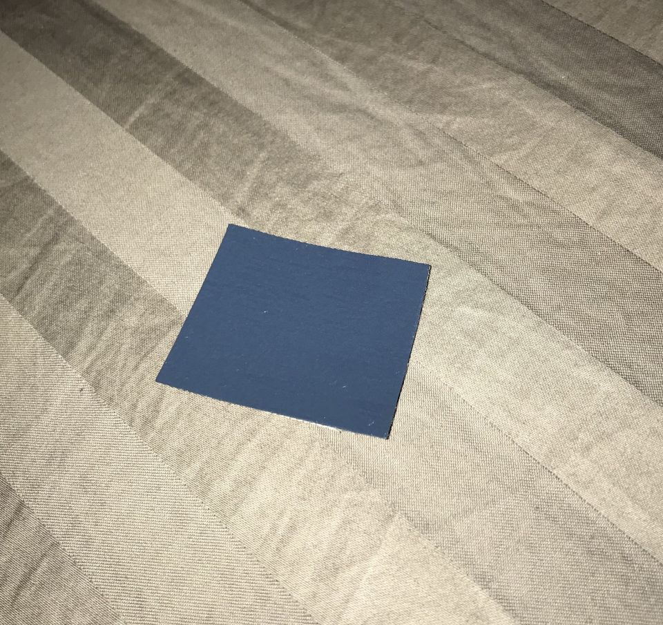 A dark blue swatch on a striped gray and beige fabric.