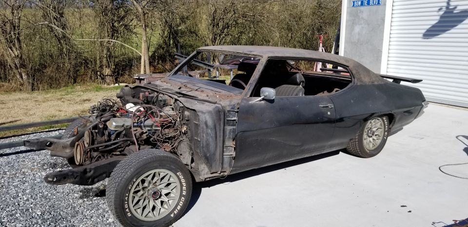 Black 1970 Pontiac Firebird Formula undergoing restoration, engine exposed, parked outside a garage.