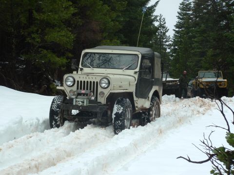 1990 Ford Bronco - A vintage Willys Jeep navigates a snowy trail, with other vehicles following in the background.