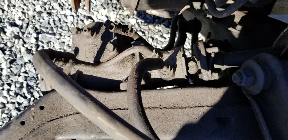 Close-up of vehicle brake caliper and suspension parts, with gravel in the background