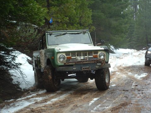 1990 Ford Bronco - This classic Ford Bronco navigates a muddy and snowy trail, with another vehicle visible in the background.