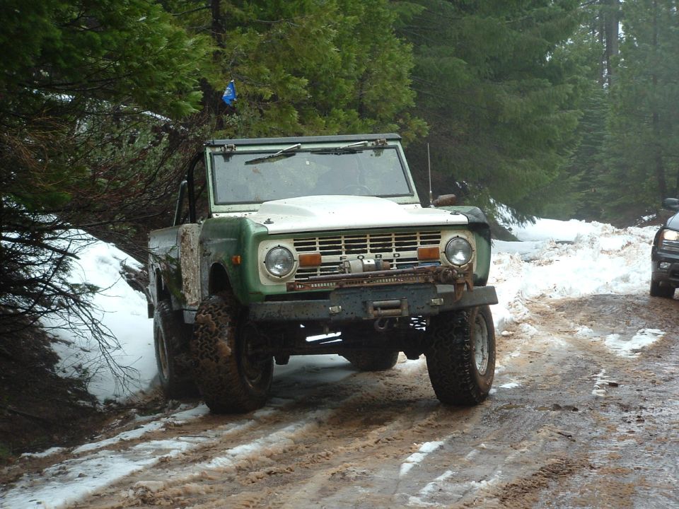 Green and white Ford Bronco with winch on snowy road