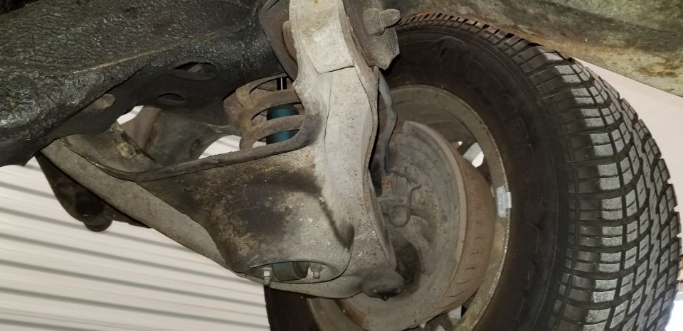Close-up of classic car front suspension, shock, spring, control arm, and brake drum.