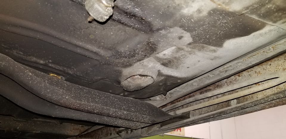 Underside of a car showing floor pan with a hole, rust, and brake lines.