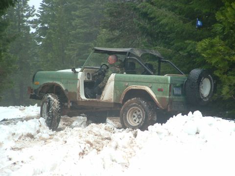 1990 Ford Bronco - A man drives a classic Ford Bronco through a snowy, wooded area.