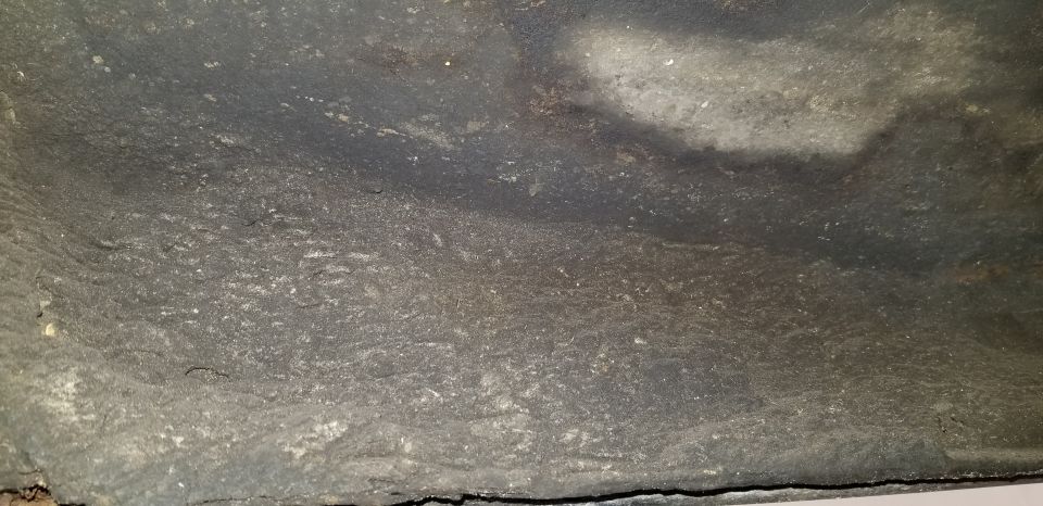 Underside of a vehicle with dark textured coating and some lighter gray patches.