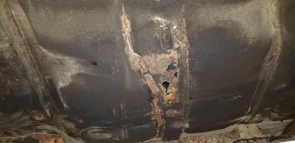 Underside of a vehicle with severe rust and holes in the floor pan.