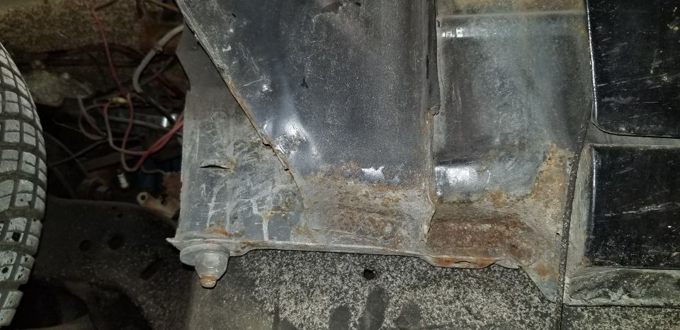 Close-up of rusted metal brackets, wiring, and a bolt under a vehicle.