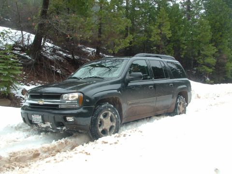 1990 Ford Bronco - A black Chevrolet Trailblazer SUV is stuck in a snowy, wooded area.