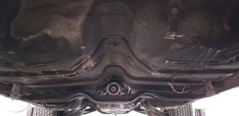 Underside of a classic car showing transmission tunnel and exhaust system with rust.