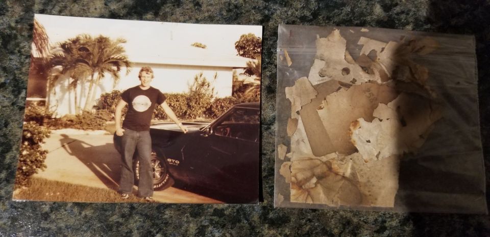 Man posing with a dark Pontiac GTO, next to a bag of old documents.