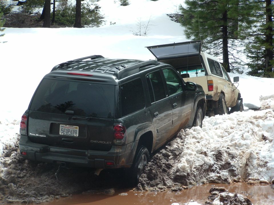 Dark SUV stuck in snow, with a tan SUV behind it with its rear door open