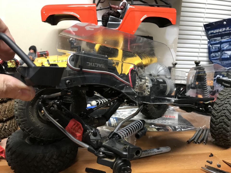 RC car chassis with clear body, orange Bronco body, tools, and parts on a wooden surface.