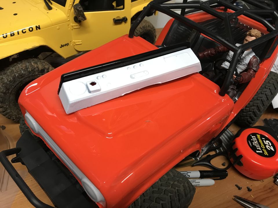 Orange RC rock crawler hood with white and black dashboard piece. Yellow RC Jeep in background.