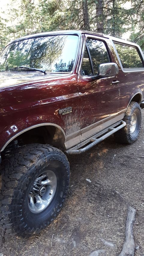 1996 Ford Bronco - The right side of a maroon Ford Bronco is shown covered in mud splashes. The vehicle has large off-road tires and metal side steps, and is…