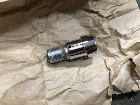 1964 Ford Fairlane - A shiny chrome fitting with threaded ends and a small hole is resting on crumpled brown paper. The fitting appears to be a component for a…