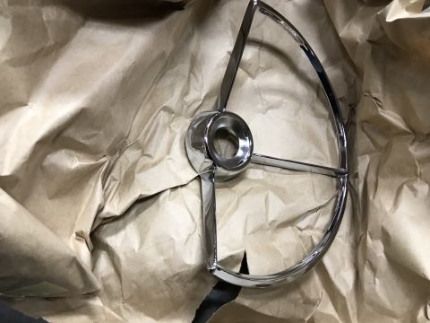 1964 Ford Fairlane - A chrome steering wheel hub and spokes are laid out on crumpled brown paper packaging. The part has a classic, retro design.