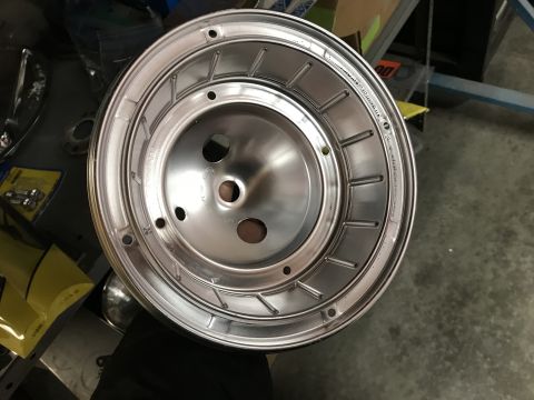 1964 Ford Fairlane - A close-up, overhead view of a shiny, silver-colored wheel cover with multiple bolt holes and a raised, ribbed design. The wheel cover is h…