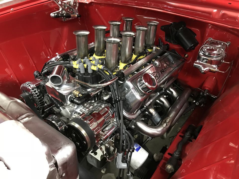 Polished chrome V8 engine with individual throttle bodies and velocity stacks in a red engine bay.