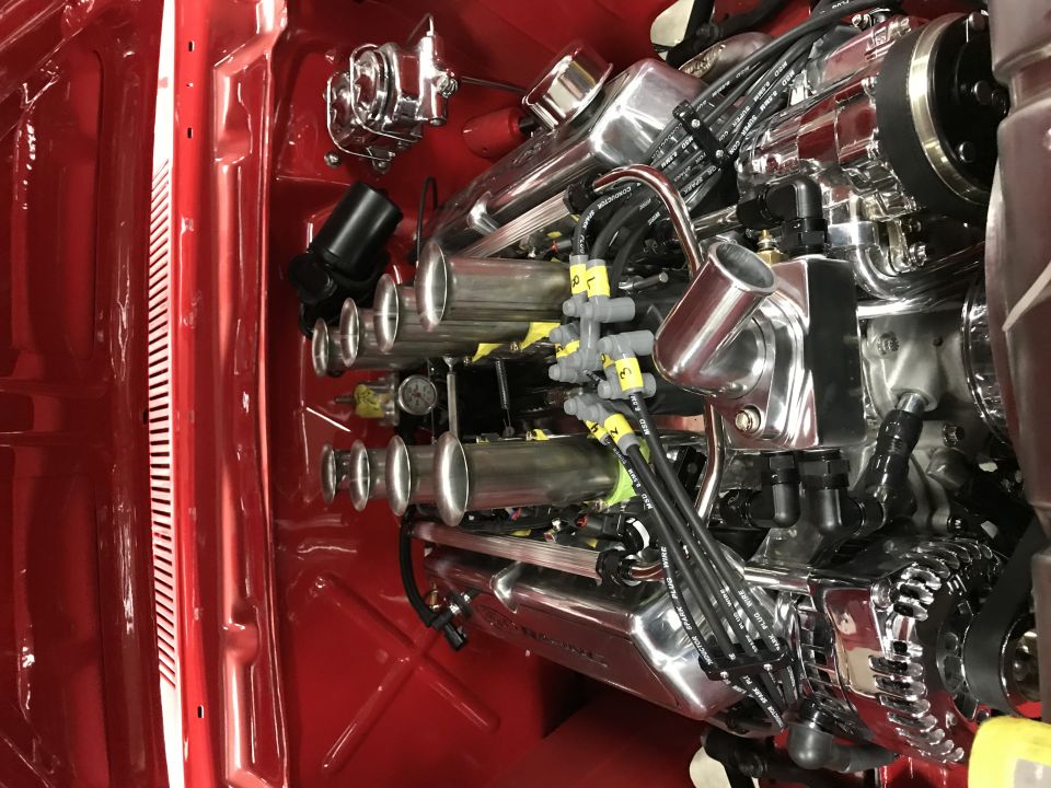 Close-up of a shiny chrome engine with individual throttle bodies in a red vehicle.