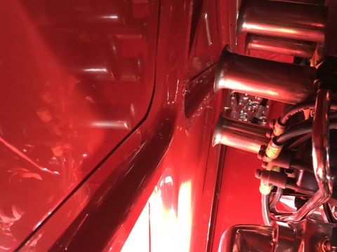 1964 Ford Fairlane - A close-up, angled view of a red vehicle's engine bay, focusing on multiple chrome intake trumpets and associated fuel lines and wiring.