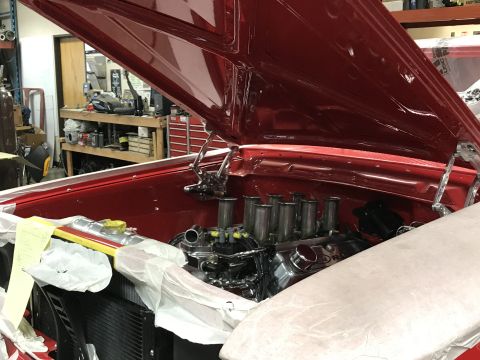 1964 Ford Fairlane - The engine bay of a red classic car is shown with the hood open. The engine features chrome components and multiple intake stacks.