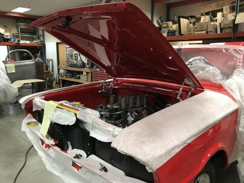 1964 Ford Fairlane - A red 1964 Ford Fairlane is shown with its hood open, revealing the engine and radiator. The car is covered in protective plastic and paper…
