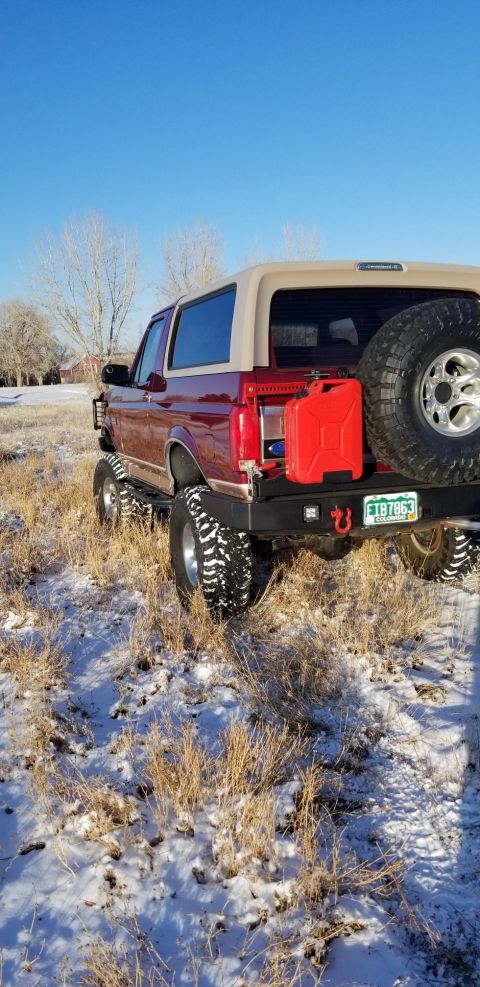 1996 Ford Bronco - A red pickup truck is viewed from the rear, parked outdoors on a sunny day.