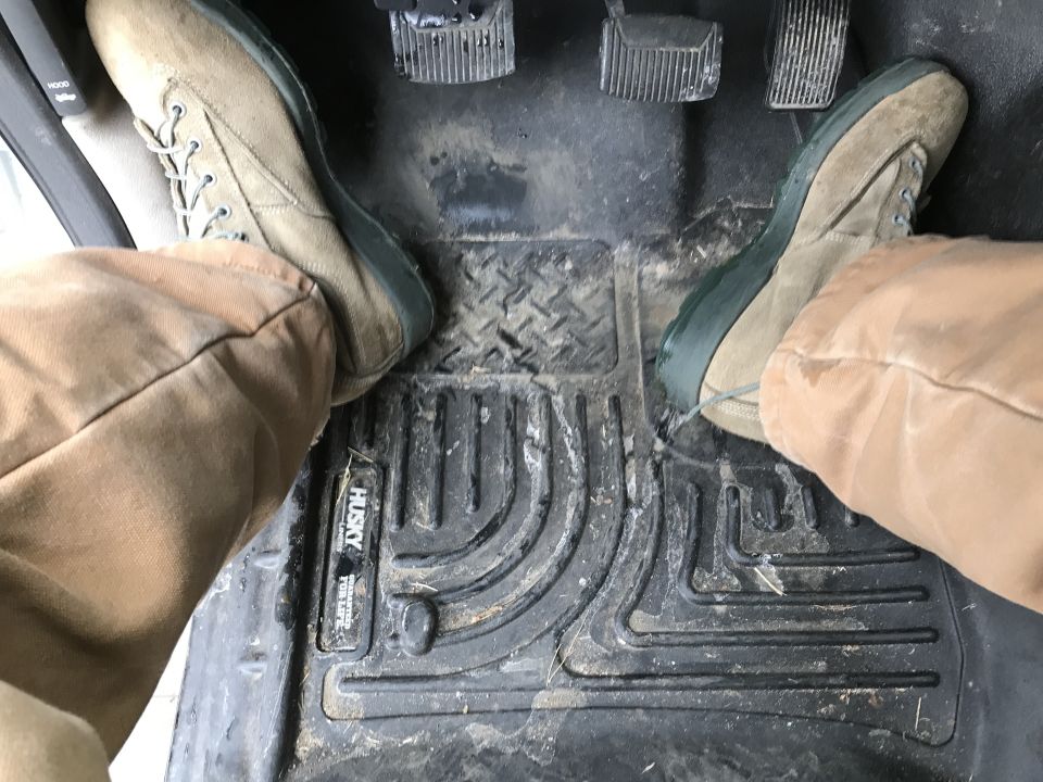 Driver's side floor pedals and Husky floor mat with two pairs of boots on them