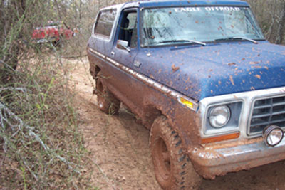 1978 Ford Bronco - A muddy 1978 Ford Bronco navigates a dirt path, with another vehicle visible in the background.