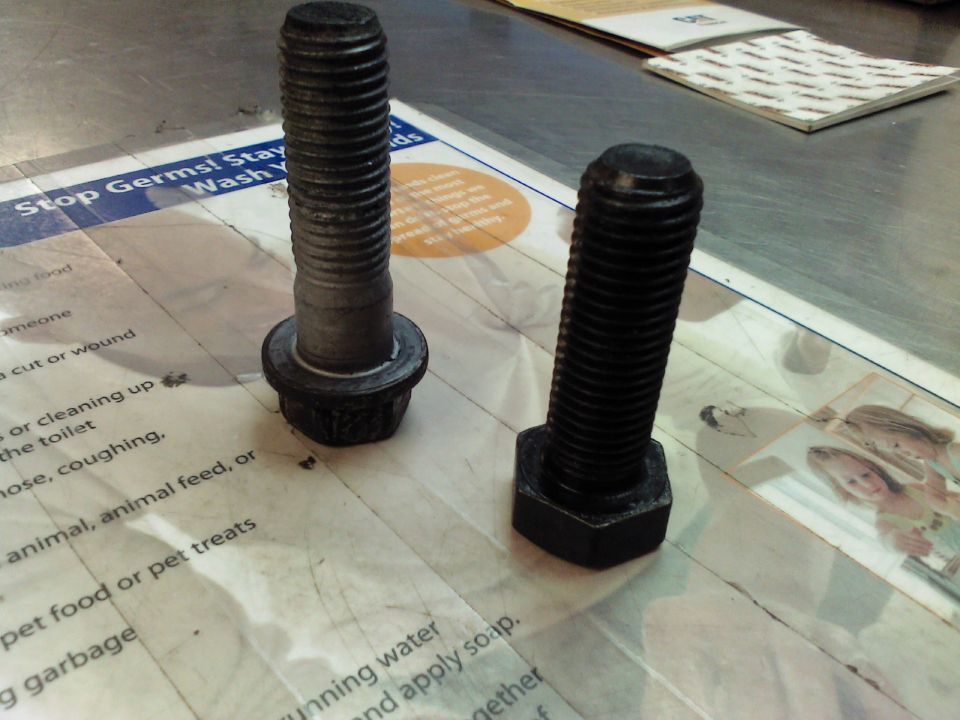 Two large bolts, one with a washer, resting on a paper with text and images