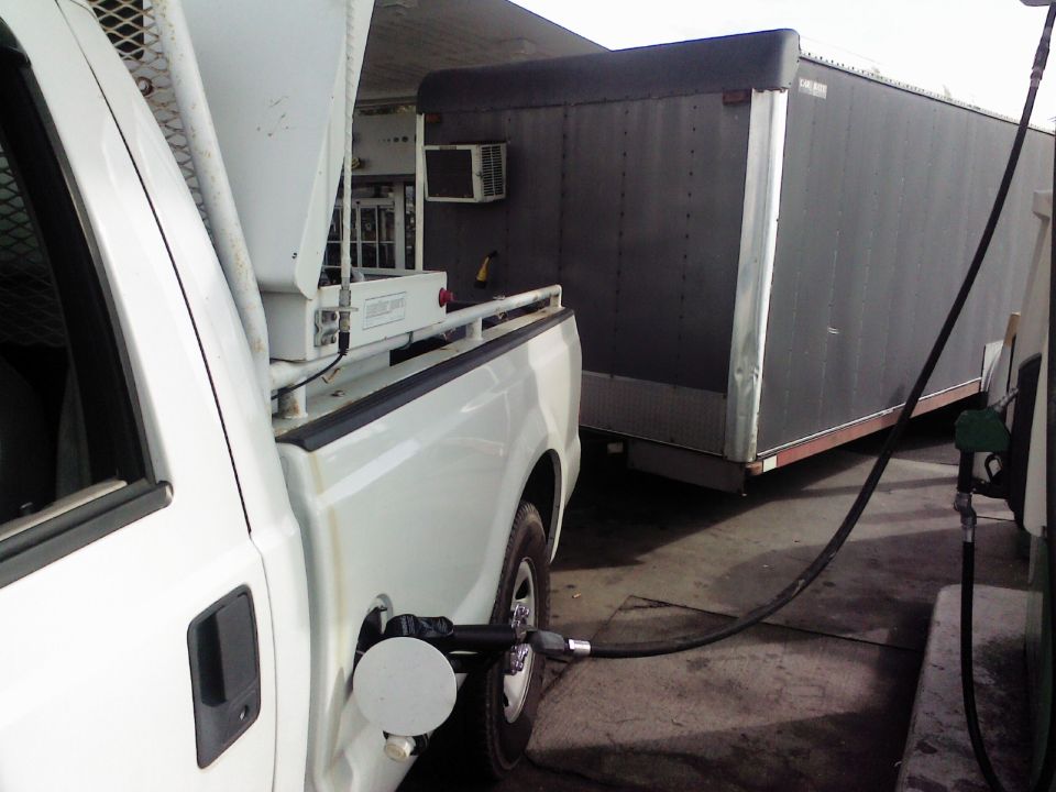 White pickup truck with a fuel nozzle in its gas tank, connected to a trailer