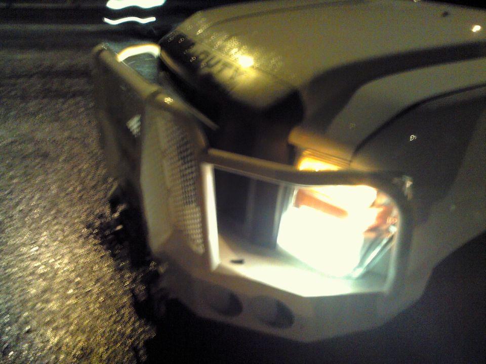 Front corner of a truck showing headlight and part of the grille. Text on hood is blurred