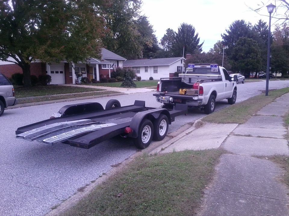 White Ford F-250 Super Duty pickup truck towing a black car hauler trailer on a residential street