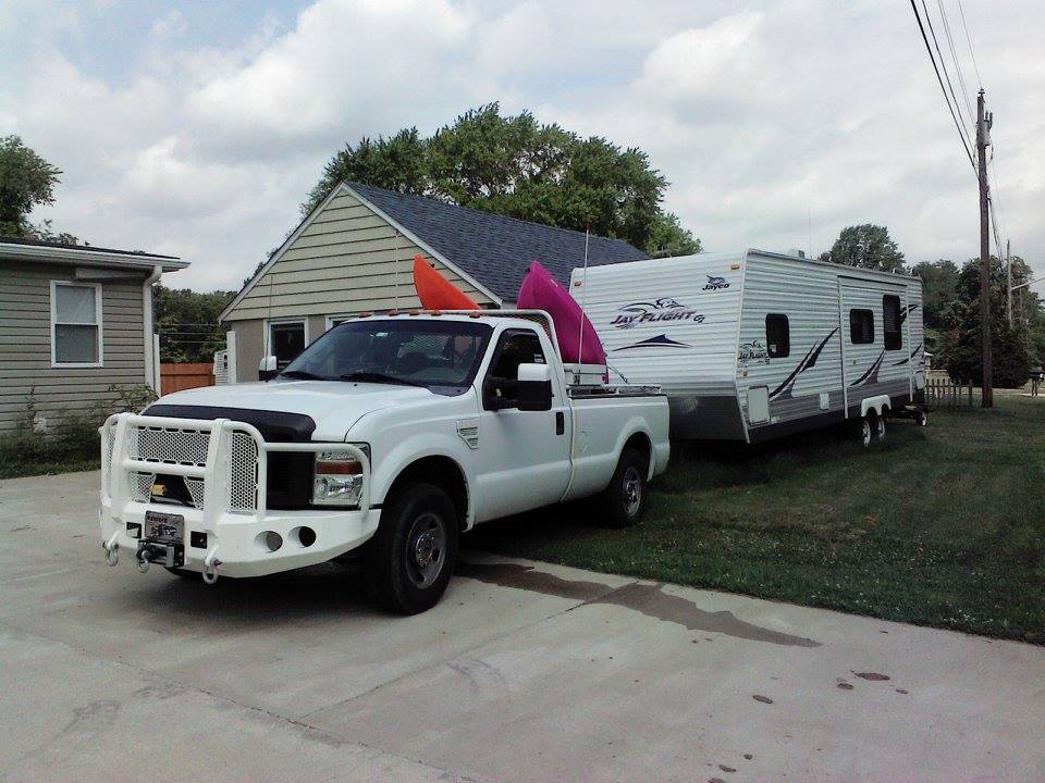White Ford F-250 Super Duty pickup truck towing a Jayco Jay Flight travel trailer, with kayaks on the roof
