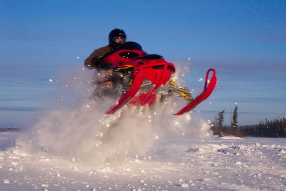 Red snowmobile jumping over snow with rider in helmet, blue sky