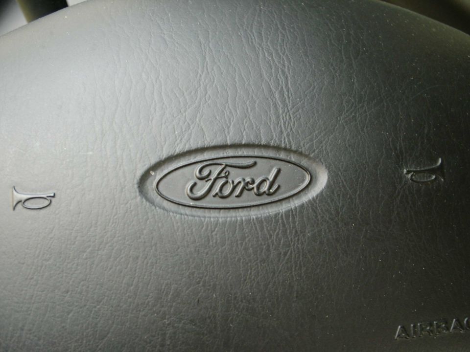 Close-up of a Ford emblem on a black steering wheel, with horn symbols on either side