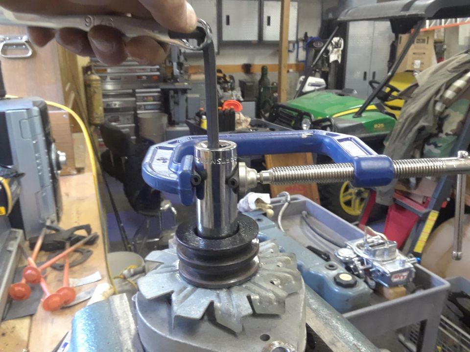 Socket wrench turning bolt on alternator pulley held by C-clamp