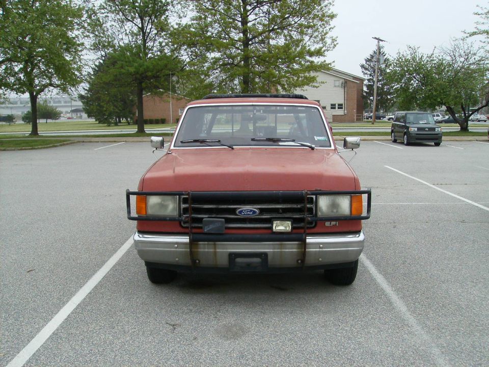 Red 1987 Ford F-150 pickup truck with a brush guard, parked in a lot. Another dark SUV is visible in the background