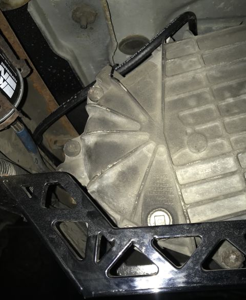 1995 Ford Bronco - A close-up view of the underside of a vehicle, focusing on the transmission or transfer case housing. A black hose runs across the top of t…