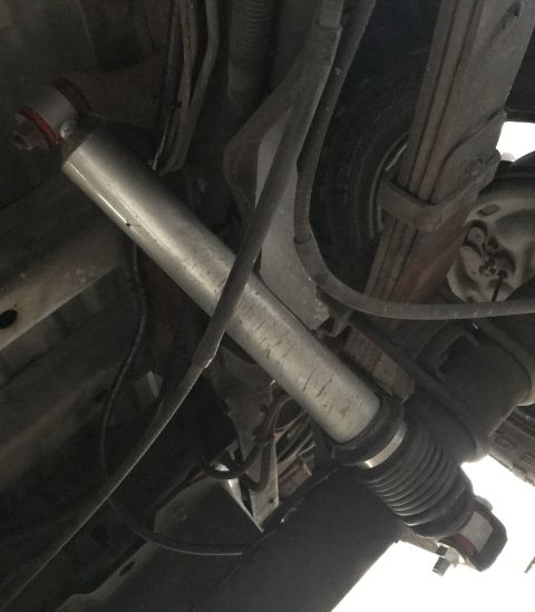 1995 Ford Bronco - Underside view of a vehicle's suspension system, featuring a silver shock absorber with red accents on one end and a black rubber boot on t…