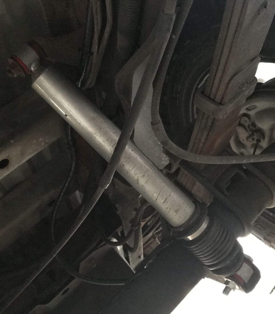 Underside of a vehicle showing a shock absorber and leaf spring.