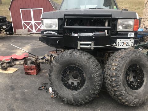 1989 Ford Bronco - A heavily modified black truck with oversized tires and a winch is parked outside a red shed. The vehicle has a Maryland license plate.