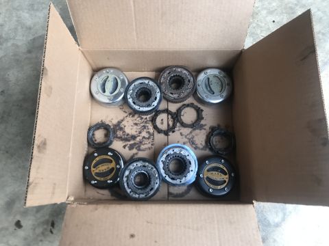 1989 Ford Bronco - A collection of vehicle drivetrain parts, including lockout hubs and gears, are laid out in a cardboard box.