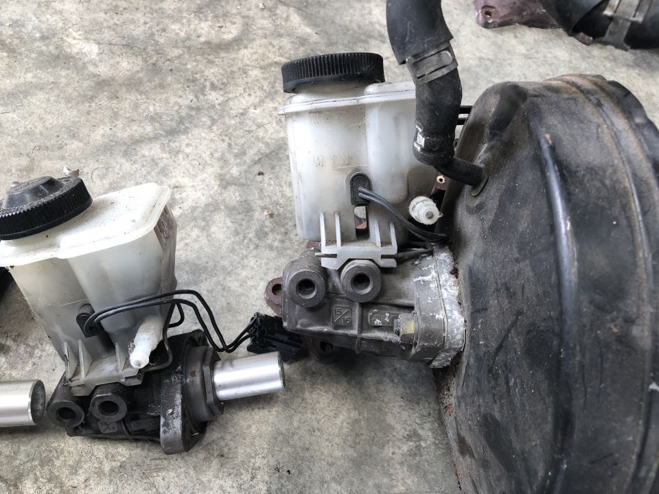Two brake master cylinders and a brake booster assembly are shown on a concrete surface