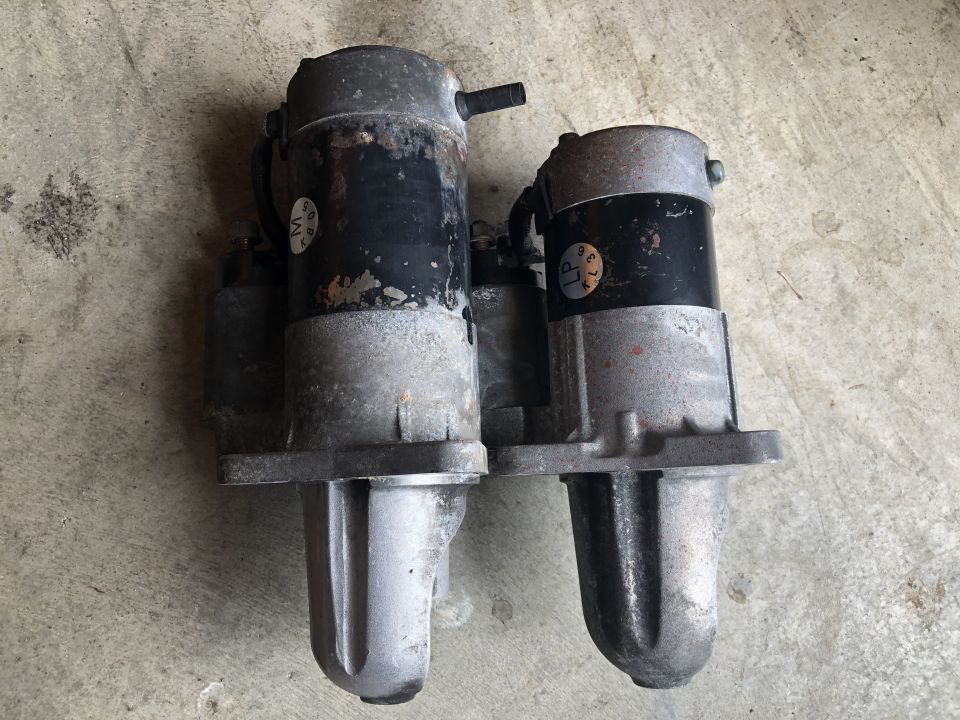 Two starter motors with labels, one with 'M' and the other with 'LP', resting on a concrete surface
